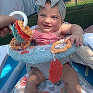 Lové is registered to the contest to win money with this photo: baby, bow, child, clothing, colorful, comfort, expression, grass, hand, headband, infant, outdoor, patterned, person, playtime, seat, smile, sock, sunlight, toy
