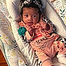 baby, infant, child, portrait, lying_down, headband, bow, pink_outfit, ruffles, pacifier, blanket, pillow, bedding, bassinet, cozy, indoors, wide_eyed, black_hair, patterned_fabric, sleepwear