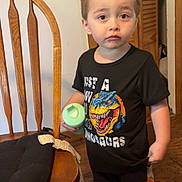 Lukas joined the competition — help win amazing prizes! black_tshirt, casual_clothing, child, curious_expression, cushion, dinosaur_graphic, door, footwear, home_interior, indoor, orange_stripes, pants, person, short_hair, sippy_cup, standing, toddler, wooden_chair, wooden_floor, young_child