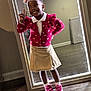 child, girl, smiling, peace_sign, mirror, pink_cardigan, heart_pattern, beige_skirt, sparkly_shoes, pink_shoes, hair_bows, pigtails, indoor, wooden_floor, reflection, happy, fashion, portrait, cute, playful