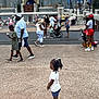 child, girl, people, theme_park, castle, stroller, walking, outdoor, daytime, crowd, shoes, shorts, tshirt, braided_hair, pavement, hats, background, family, casual_clothing, tourist