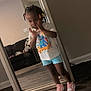 child, mirror, indoor, floor, tshirt, shorts, sneakers, pose, hair_beads, living_room, sofa, wood_floor, reflection, person, young, cute, standing, furniture, casual, home