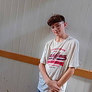 Killian a rejoint le concours — aidez-le/la à gagner de superbes lots ! blue_jeans, boy, casual_clothing, child, glasses, hands, indoor, leaning, light, person, portrait, relaxed, short_hair, shy, smile, standing, wall, white_tshirt, wooden_strip, young