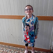 Ines a rejoint le concours — aidez-le/la à gagner de superbes lots ! cartoon_characters, casual_clothing, child, dress, footwear, girl, glasses, happy, indoor, leggings, light, patterned_floor, person, smile, sneakers, standing, tiled_floor, wall, wood_trim, young