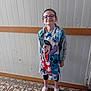 cartoon_characters, casual_clothing, child, dress, footwear, girl, glasses, happy, indoor, leggings, light, patterned_floor, person, smile, sneakers, standing, tiled_floor, wall, wood_trim, young