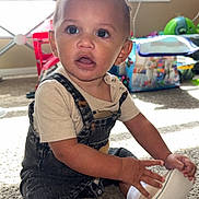 Isaac joined the competition — help win amazing prizes! toddler, child, indoor, carpet, denim_overalls, beige_shoes, socks, face, eyes, hand, toy, window, air_conditioner, natural_light, floor, expression, curiosity, clothing, person, room