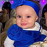 baby, blue_dress, blue_headband, child, curly_hair, cute, decor, event, face, flower_accessory, hand, happy, indoor, lighting, party, people, portrait, seated, smile, white_shirt