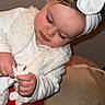 baby, beige_background, child, cozy, cushion, cute, expression, face, focused, hands, headband, indoor, long_eyelashes, playing, portrait, red_skirt, tissue, toddler, white_bow, white_clothing