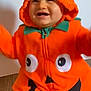 baby, child, pumpkin_costume, orange, hood, striped_leggings, smiling, happy, cute, indoor, floor, costume, holiday, festive, joyful, toddler, playful, face, person, sitting