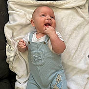 Gwylym is registered to the contest to win money with this photo: baby, infant, smiling, overalls, clothing, peter_rabbit, blanket, soft_texture, happy, cute, face, hand, fingers, lying_down, indoor, child, light_blue, white, comfort, couch