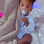 Jahmir is registered to the contest to win money with this photo: baby, pacifier, blanket, child, indoors, curly_hair, puffs, sitting, cozy, soft_fabric, white_clothing, cute, infant, comfort, bedroom, nap_time, young_child, portrait, face, hand