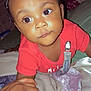 Jahmir is registered to the contest to win money with this photo: baby, child, infant, hand, blanket, red_shirt, curly_hair, indoors, face, wide_eyes, skin, person, holding_hand, crawling, expression, cute, bedroom, young_child, closeup, portrait