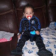 Cire joined the competition — help win amazing prizes! toddler, child, pacifier, sippy_cup, tracksuit, black_shoes, blanket, couch, leather_couch, indoor, clothing, baby, person, sitting, blue, red, toy, wipes, fabric, home