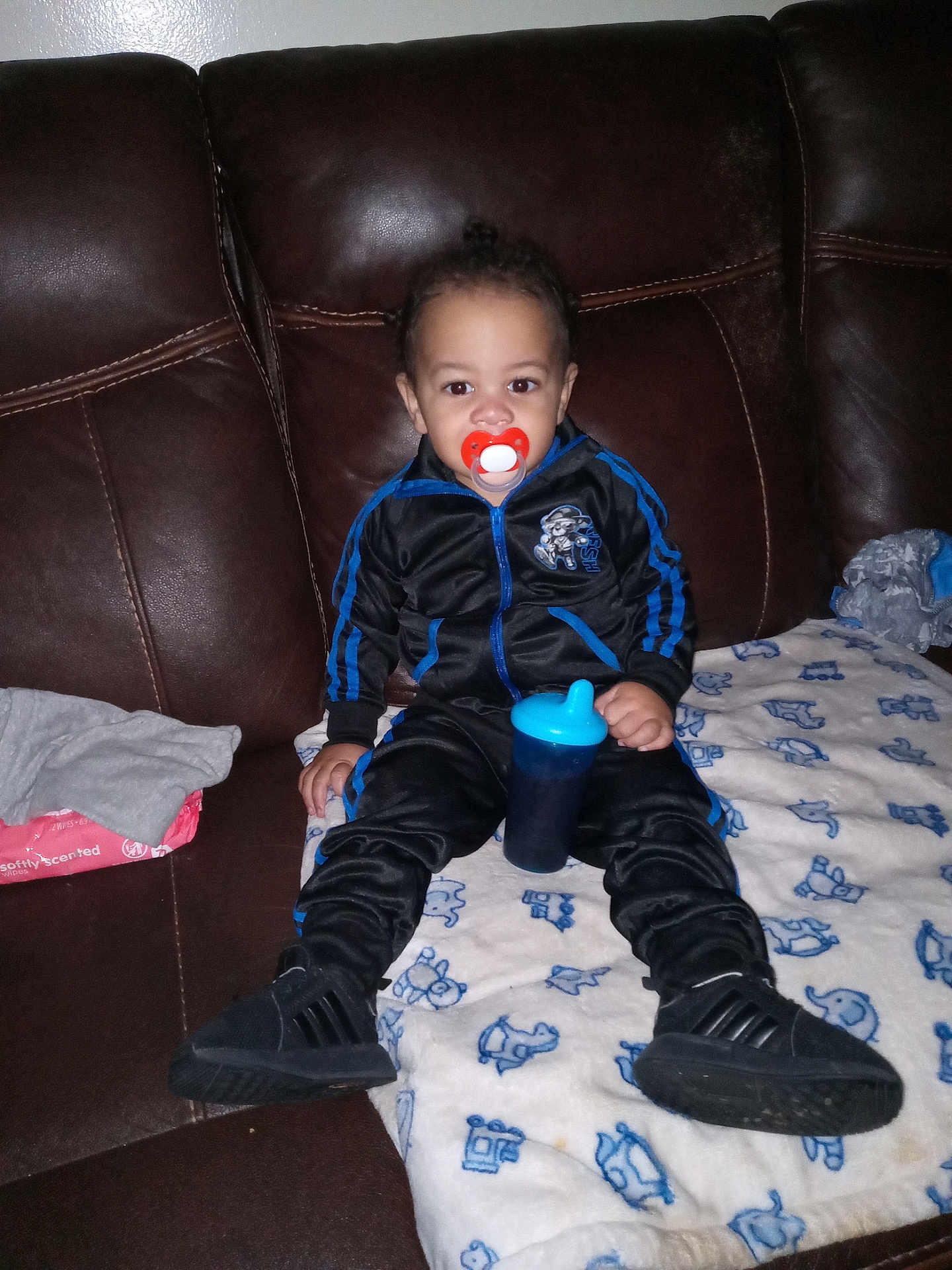 Cire joined the competition — help win amazing prizes! toddler, child, pacifier, sippy_cup, tracksuit, black_shoes, blanket, couch, leather_couch, indoor, clothing, baby, person, sitting, blue, red, toy, wipes, fabric, home
