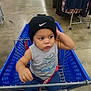 Malachi is registered to the contest to win money with this photo: toddler, child, shopping_cart, blue_cart, nike_beanie, clothing, store, retail, floor, concrete, rack, clothes, shorts, sleeveless_shirt, cute, curious, indoors, person, baby, casual