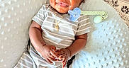 Tylan is registered to the contest to win money with this photo: baby, infant, smiling, striped_clothing, pacifier, cushion, textured_fabric, patterned_rug, sock, jewelry, happy, indoors, child, cute, portrait, laying_down, hand_gesture, head, face, person