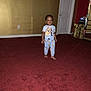 toddler, child, pajamas, barefoot, red_carpet, indoor, door, wall, yellow_wall, red_wall, small_table, electronic_device, carpet, person, foot, standing, room, furniture, clothing, home