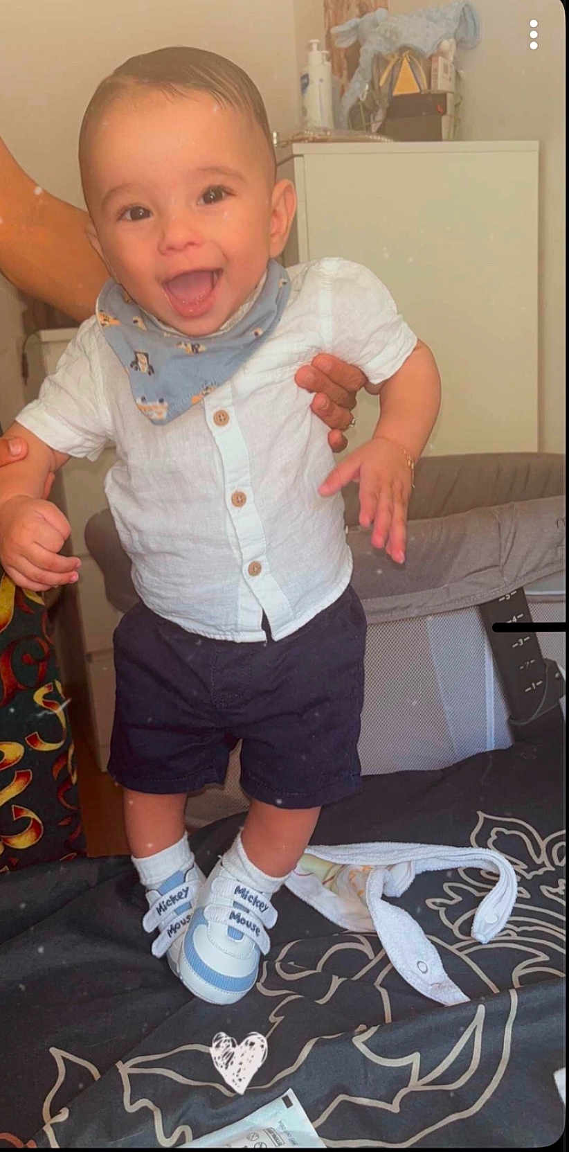 Kenan participe au concours pour gagner de l'argent avec cette photo : baby, bed, blanket, child, clothing, cute, fabric, footwear, furniture, hand, happy, indoor, mickey_mouse_shoes, navy_shorts, person, smiling, socks, standing, toddler, white_shirt