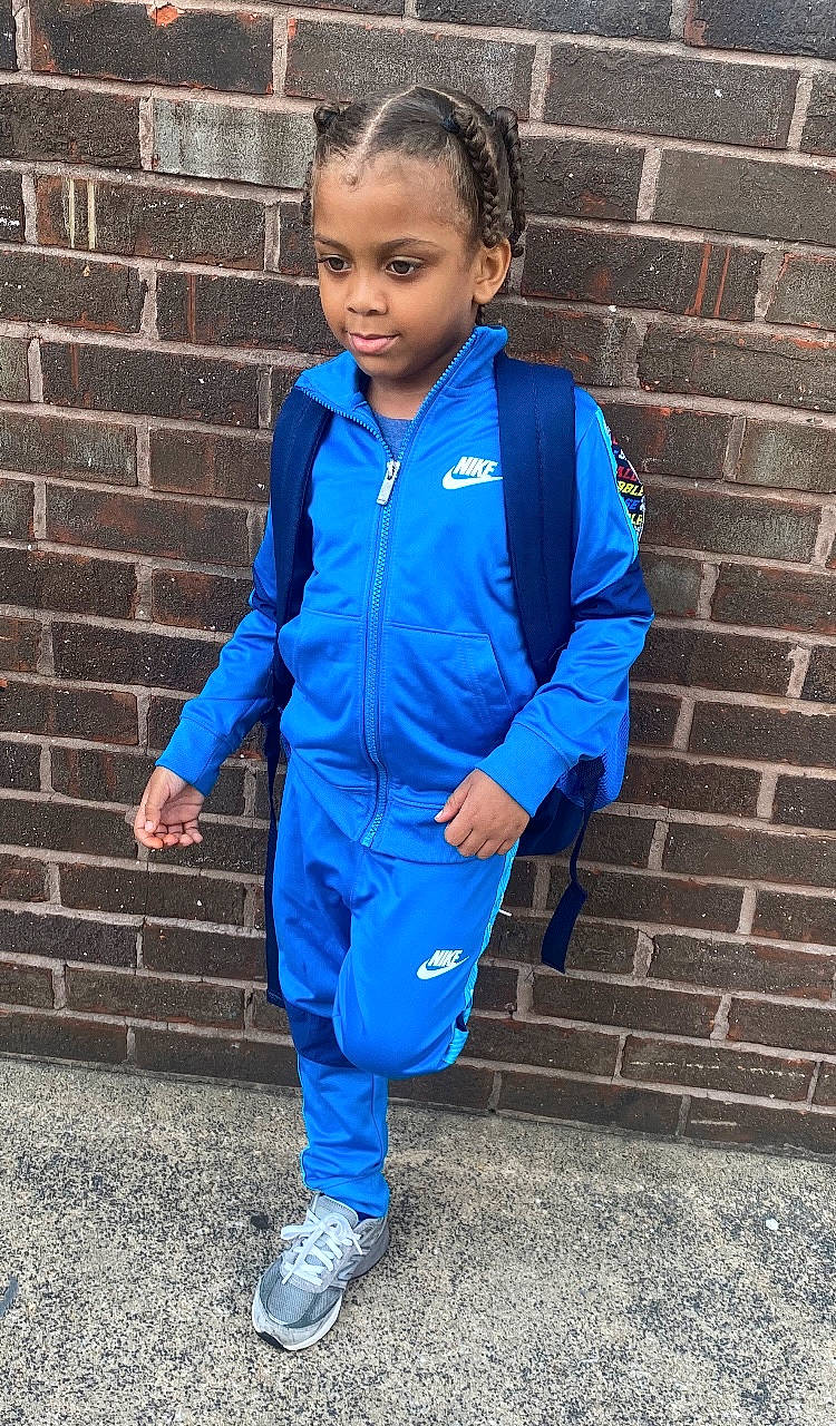 Kareem is registered to the contest to win money with this photo: blazer, blue, brick, brickwork, child, clothing, collar, denim, electric_blue, face, formal_wear, hair, happy, person, school_uniform, sleeve, smile, sportswear, sweatpant, toddler