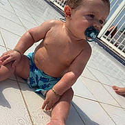 Lenzo participe au concours pour gagner de l'argent avec cette photo : baby, child, pacifier, water, wet_skin, poolside, tiled_floor, sunlight, shadow, bracelet, blue_swim_diaper, outdoor, summer, sitting, cute, infant, skin, foot, hand, face