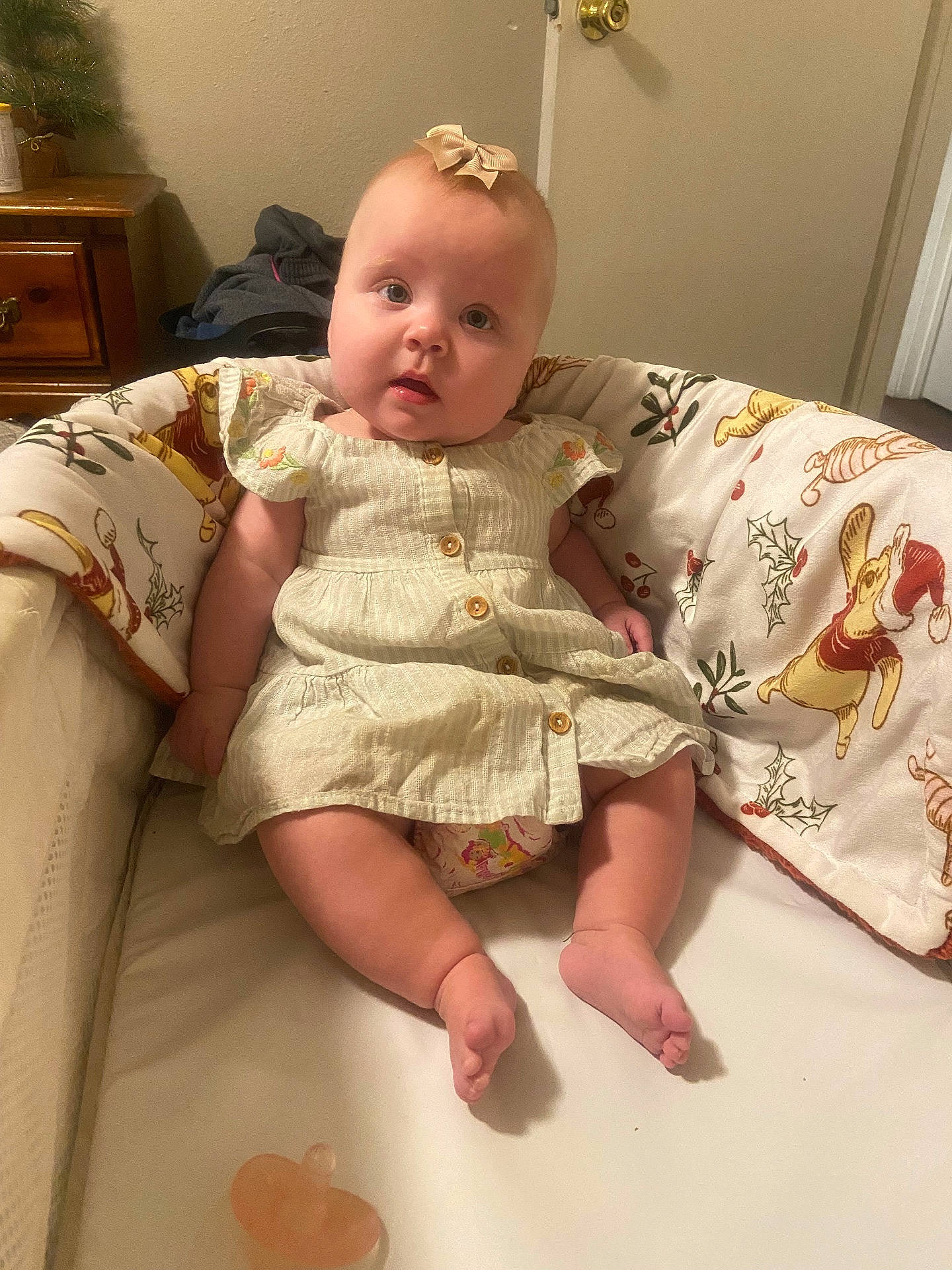 baby, blanket, bow, child, chubby, comfort, crib, cute, decor, door, dress, expression, face, furniture, holiday, indoors, infant, pacifier, sitting, skin