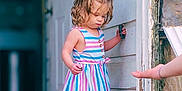 Bray joined the competition — help win amazing prizes! barefoot, building, child, curious, curly_hair, daylight, door, exploring, hand, old_wood, outdoor, person, playful, standing, striped_dress, summer, toddler, wall, wooden_porch, young_child