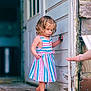child, toddler, barefoot, striped_dress, curly_hair, door, wooden_porch, hand, exploring, outdoor, building, wall, old_wood, summer, daylight, person, young_child, curious, standing, playful
