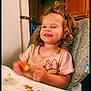 child, curly_hair, eating, face, food, hands, happy, high_chair, home, indoor, kitchen, meal, messy, minnie_mouse, person, plate, shirt, smiling, toddler, young_child