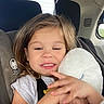 car, car_interior, car_seat, casual_clothing, child, cute, daylight, face, hair, hand, person, plush_toy, safety, seatbelt, smile, stuffed_animal, travel, window, winking, young_child