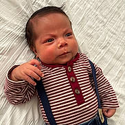 Ivan is registered to the contest to win money with this photo: baby, infant, striped_shirt, suspenders, denim, clothing, lying_down, white_blanket, cute, face, hand, portrait, newborn, child, young, expression, indoor, apparel, person, skin