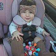 Vianney joined the competition — help win amazing prizes! baby, infant, child, car_seat, vehicle, headband, bow, pink, portrait, face, eyes, smiling, clothing, onesie, socks, toy, colorful, harness, seated, indoor