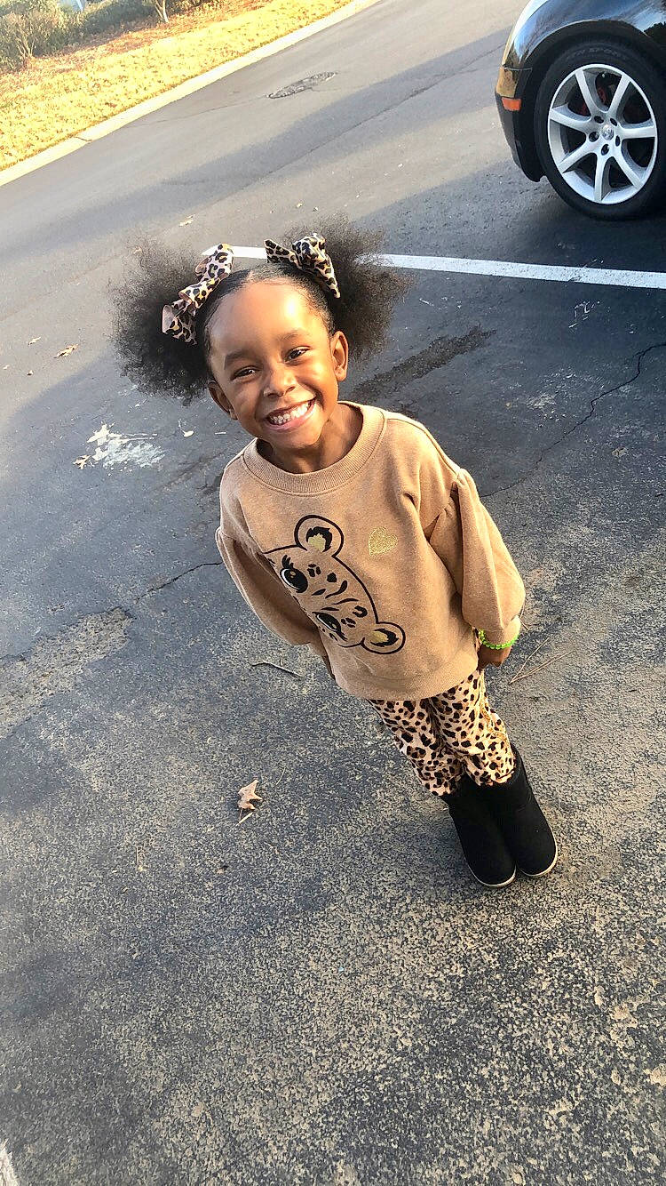 London is registered to the contest to win money with this photo: asphalt, automotive_tire, black, cool, eye, grass, happy, joy, person, personal_luxury_car, road, road_surface, sidewalk, smile, street, t_shirt, tints_and_shades, tire, toddler, vehicle_door