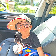 Jayden Reyes is registered to the contest to win money with this photo: baseball_cap, black_shirt, boy, car_door, car_interior, casual, child, glasses, house, playful, portrait, reflection, rocket, seat, seatbelt, smile, sunlight, toy, tree, window
