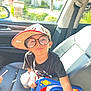 baseball_cap, black_shirt, boy, car_door, car_interior, casual, child, glasses, house, playful, portrait, reflection, rocket, seat, seatbelt, smile, sunlight, toy, tree, window