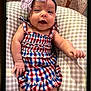baby, infant, smiling, dress, headband, bow, cushion, checked_pattern, happy, child, cute, portrait, indoors, young, skin, person, clothing, baby_girl, resting, closeup