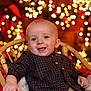 baby, child, plaid_shirt, wicker_chair, holiday_lights, bokeh, smiling, portrait, indoor, festive, warm_lighting, cute, happy, infant, cozy, red, green, beige, background, celebration