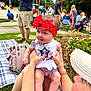 Avalyn joined the competition — help win amazing prizes! baby, child, red_bow, headband, patriotic_clothing, outdoor, people, grass, picnic_blanket, backpack, adult, festival, crowd, summer, smile, legs, holding, hat, nature, celebration