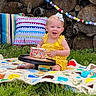 Porter joined the competition — help win amazing prizes! baby, child, yellow_dress, birthday_cake, outdoor, grass, crocheted_blanket, pillows, wood_logs, garland, colorful, smiling, happy, celebration, party, cute, headband, food, sitting, person