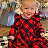 baby, child, smiling, red_dress, checkered_pattern, sitting, blanket, holiday, christmas_tree, lights, indoor, cute, festive, happy, person, portrait, floor, decor, ribbon, black_sock