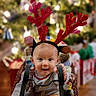 Porter is registered to the contest to win money with this photo: baby, child, reindeer_ears, holiday, christmas_tree, basket, indoor, festive, decorations, lights, wood_floor, curious, cute, smiling, seasonal, celebration, home, holiday_spirit, infant, cozy