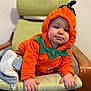 Leo a rejoint le concours — aidez-le/la à gagner de superbes lots ! toddler, child, pumpkin_costume, orange, green_chair, cushion, indoors, cute, smiling, costume, baby, hands, face, hood, wooden_chair, person, seat, clothing, expression, plush