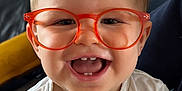 Leo participe au concours pour gagner de l'argent avec cette photo : toddler, child, glasses, orange_glasses, happy, smiling, indoor, portrait, baby, clapping, hands, face, cute, person, white_shirt, buttoned_shirt, short_hair, light_skin, seated, cozy