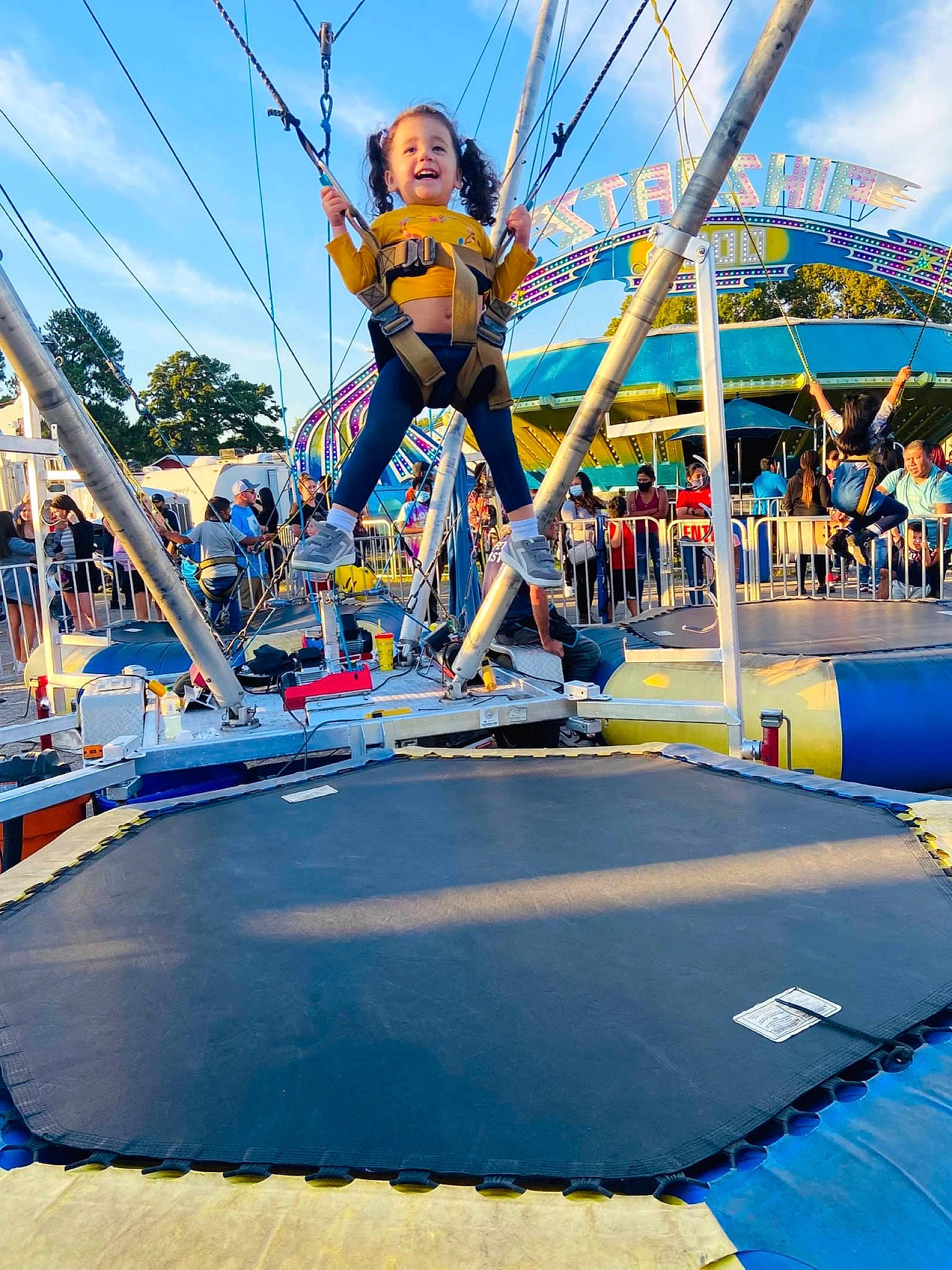 Lilian is registered to the contest to win money with this photo: blue, city, cloud, electric_blue, entertainment, event, fun, leisure, nonbuilding_structure, outdoor_play_equipment, person, playground, pole, public_event, recreation, sky, smile, sports, sports_equipment, trampoline