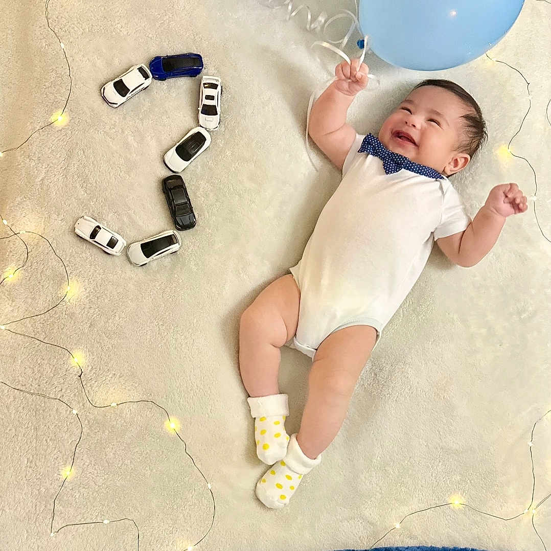 Elian Sebastian is registered to the contest to win money with this photo: baby, balloons, birthday, blanket, blue, celebration, child, cute, decorations, happy, indoor, infant, lights, number_two, playful, polka_dot_socks, smiling, soft_texture, toy_cars, white_onesie