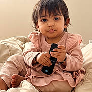 Vamika joined the competition — help win amazing prizes! toddler, child, remote_control, pink_clothing, bed, blanket, indoor, portrait, cute, pout, sitting, cozy, soft_light, expression, person, baby, home, casual, hands, foot