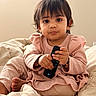 toddler, child, remote_control, pink_clothing, bed, blanket, indoor, portrait, cute, pout, sitting, cozy, soft_light, expression, person, baby, home, casual, hands, foot