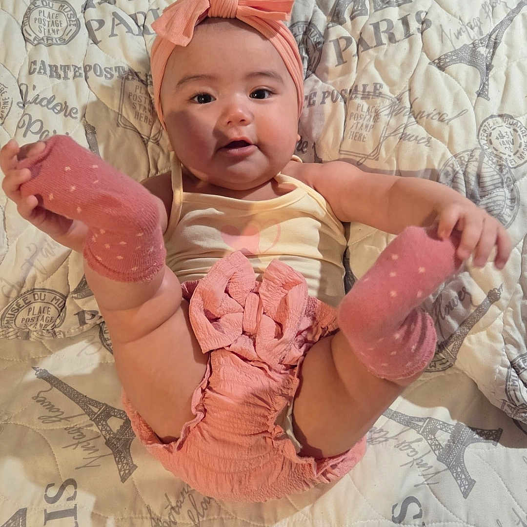 Kathy joined the competition — help win amazing prizes! baby, infant, pink_socks, headband, smiling, cute, lying_down, playful, blanket, quilt, patterned, paris_theme, indoor, child, adorable, happy, legs_up, clothing, person, portrait