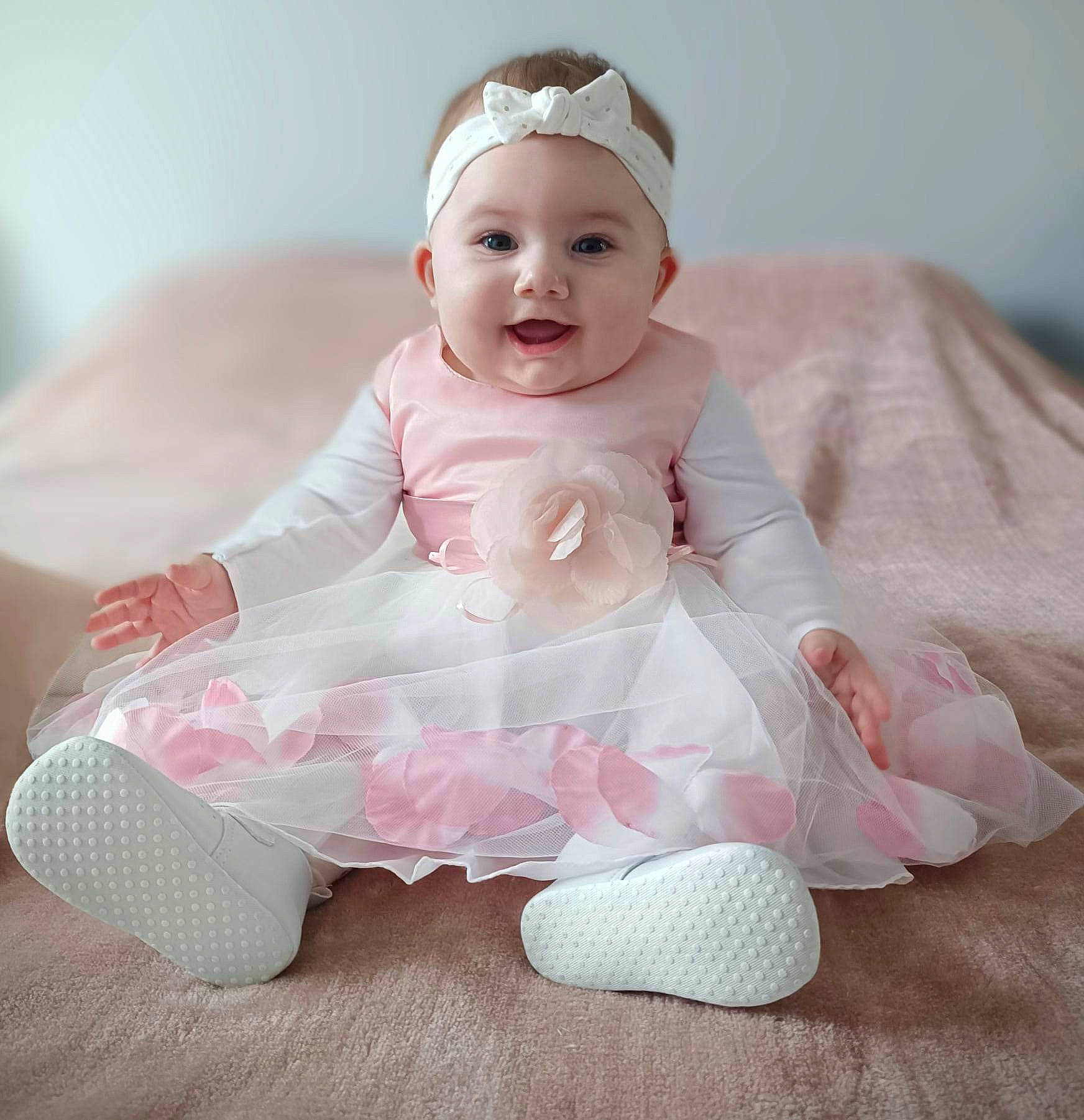 Lounnah participe au concours pour gagner de l'argent avec cette photo : baby, baby_products, baby_toddler_clothing, cheek, dress, face, fashion_accessory, hair_accessory, happy, headband, headpiece, headwear, joy, pattern, peach, person, pink, ruffle, sitting, sleeve
