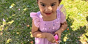 Isabella is registered to the contest to win money with this photo: child, girl, pink_dress, bow, confetti, grass, outdoor, sunlight, eggshells, broken_eggs, celebration, happy, smiling, holding, footwear, party, spring, festive, colorful, nature