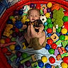 toddler, child, ball_pit, toys, balls, inflatable_ring, colorful, play, indoor, smiling, happy, cute, wooden_blocks, stuffed_toy, soccer_ball, basketball, clothing, shorts, shirt, person